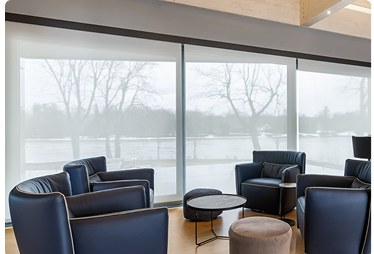 Motorized sheer shades across a wall of windows in a lakeside sitting room