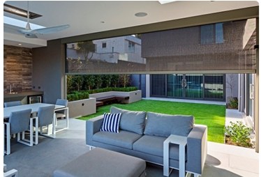 Outdoor motorized shades enclosing a patio beside a kitchen and garden